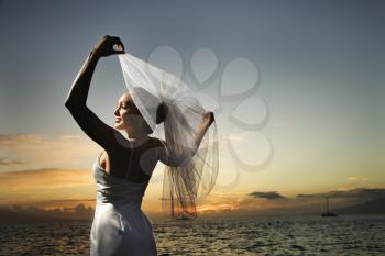Royalty Free Photo of Young Bride Holding Out Her Veil on a Beach
