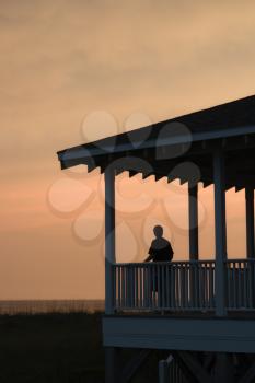 Royalty Free Photo of a Boy on a Beachfront Porch Silhouetted at Sunset