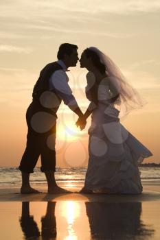 Royalty Free Photo of a Bride and Groom Holding Hands and Kissing Barefoot on a Beach at Sunset