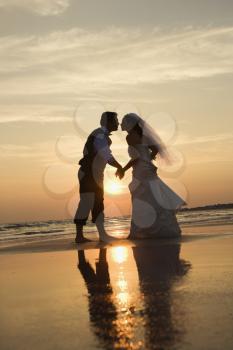 Caucasian prime adult male groom and female bride holding hands and kissing barefoot on beach at sunset.