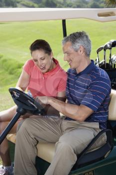 Royalty Free Photo of a Male and Female in a Golf Cart Pointing at a Score Card