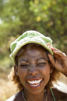 MId-adult African American female smiling with hand on cap and squinted eyes.