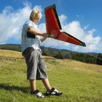 Pre-teen Caucasian male preparing to fly remote controlled airplane on grassy knoll.