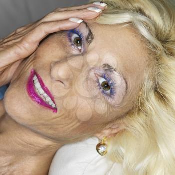 Royalty Free Photo of a Portrait of a Tan Blonde Middle-aged Woman Wearing Lots of Makeup With Hand on Her Face Smiling