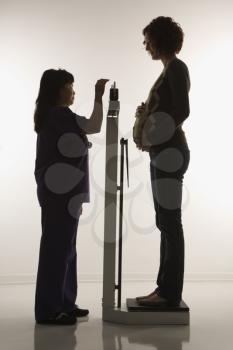 Royalty Free Photo of a Pregnant Woman Being Weighed by a Nurse