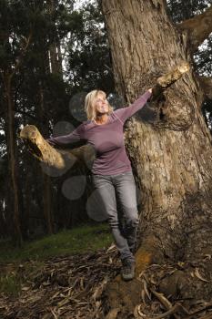 Royalty Free Photo of a Middle-aged Woman Smiling Leaning on a Tree in the Forest