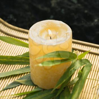 Royalty Free Photo of a Burning candle on bamboo mat with bamboo leaves