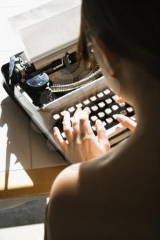 Royalty Free Photo of a Woman Sitting at a Kitchen Table Typing on a Typewriter