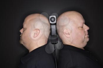 Caucasian mid adult identical twin men standing back to back with telephone balancing between them.
