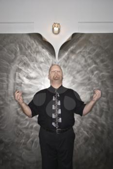 Caucasian bald mid adult men standing with arms outstretched and eyes closed in a meditative position.