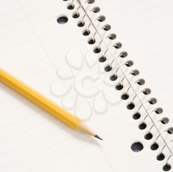Sharp pencil placed on open spiral bound notebook.