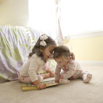 Royalty Free Photo of Little Girls Sitting on the Floor Looking at a Book