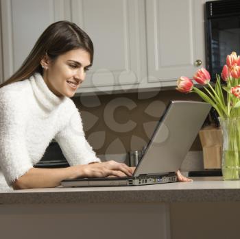 Royalty Free Photo of a Woman Typing on a Laptop in Her Kitchen
