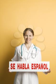 Royalty Free Photo of a Female Doctor Holding Up a Se Habla Espanol Sign Smiling