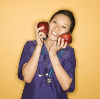 Royalty Free Photo of a Female Doctor Holding Apples Up to Her Face against Smiling 