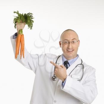 Caucasian mid adult male physician holding and pointing to bunch of carrots.