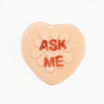 Orange candy heart that reads ask me against white background.