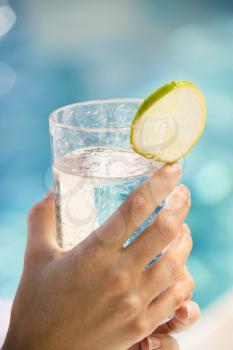Royalty Free Photo of a Woman's Hand Holding a Drink Glass Garnished With a Lime Slice Next to a Pool