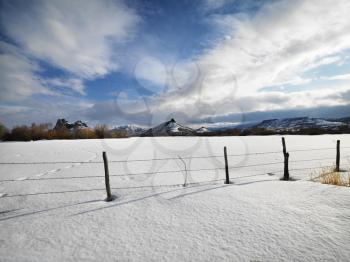 Barbed wire fence with snow covered ground and mountains in background.