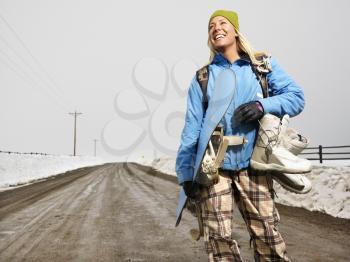 Royalty Free Photo of a Woman Wearing Winter Clothes Standing on a Muddy Dirt Road Holding a Snowboard and Boots