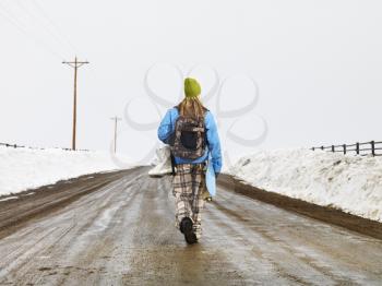 Royalty Free Photo of a Woman in Winter Clothes Standing on a Muddy Dirt Road Holding a Snowboard and Boots