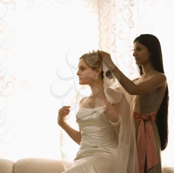 Royalty Free Photo of a Bridesmaid Placing a Veil on a Bride