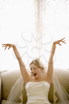 Royalty Free Photo of a Bride on a Love Seat With Arms Raised and Joyful Expression