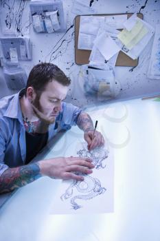Caucasian male tattoo artist drawing tattoo on light table.