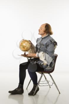 Royalty Free Photo of William Shakespeare in Period Clothing Sitting in a School Desk Looking at a Globe