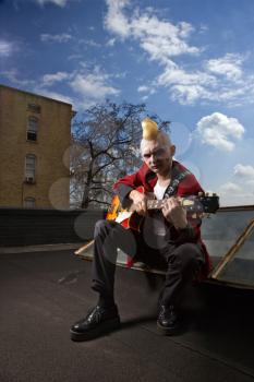 Royalty Free Photo of a Male Punk Playing Guitar With a Building in the Background