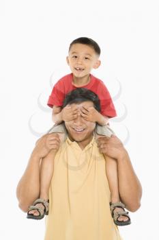 Royalty Free Photo of a Boy Sitting on His Father's Shoulders With Hands Over His Eyes