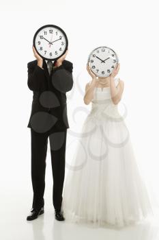 Royalty Free Photo of a Bride and Groom Covering Their Faces With Clocks
