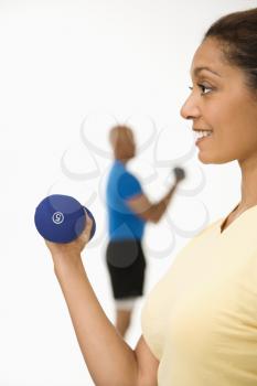 Royalty Free Photo of a Woman Exercising Using Dumbbells With a Man in the Background