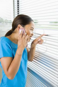 Royalty Free Photo of a Preteen Girl Looking Through the Blinds While Talking on a Cellphone