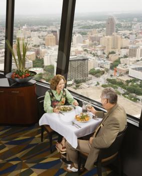 Royalty Free Photo of an Older Couple Dining in a Fancy Restaurant by a Window With a Rooftop View of Urban Landscape