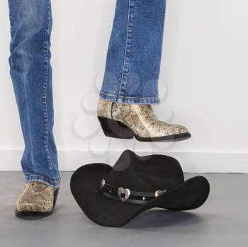 Royalty Free Photo of a Woman Wearing Snakeskin Cowboy Boots About to Stomp on a Black Cowboy Hat