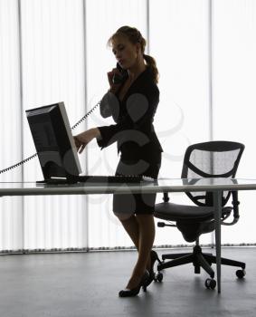 Royalty Free Photo of a Businesswoman Standing at a Computer Desk Talking on the Telephone