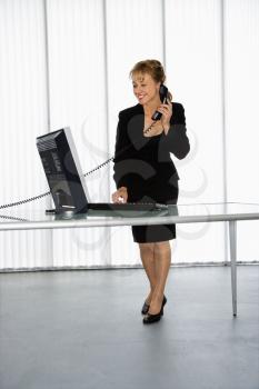 Royalty Free Photo of a Businesswoman Standing at a Desk Talking on a Telephone