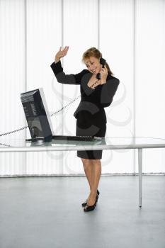 Royalty Free Photo of a Businesswoman Standing at the Computer Desk Waving While on the Telephone
