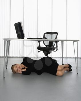 Royalty Free Photo of a Businesswoman Sleeping on a Floor Under a Computer Desk