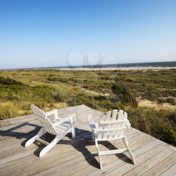 Two adirondack chairs on wooden deck overlooking beach at Bald Head Island, North Carolina.