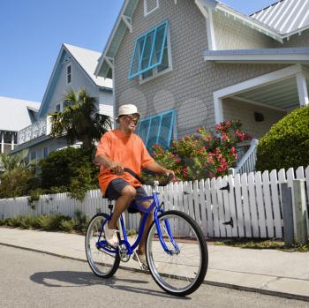Royalty Free Photo of a Man Bicycling Down a Street Next to Homes