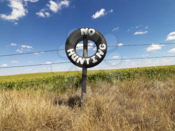 Royalty Free Photo of a Barbed Wire Fence With a Tire Reading No Hunting in Front of a Agricultural Field