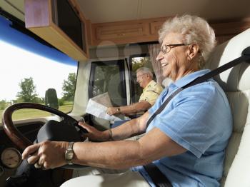 Royalty Free Photo of an Older Woman Driving an RV and Smiling While Her Husband Reads a Map in the Passenger Seat