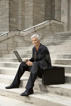 Royalty Free Photo of a Businessman Sitting on Steps With His Laptop