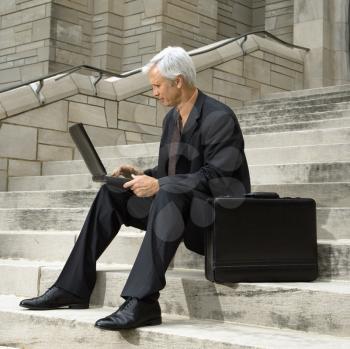 Royalty Free Photo of a Businessman Sitting on Steps Outdoors With a Laptop and Briefcase