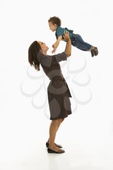 Side view of mid adult African American mom lifting happy toddler son into air above head.
