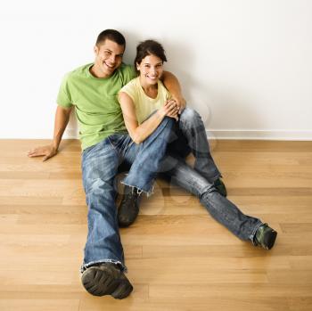 Royalty Free Photo of an Attractive Couple Sitting Close on a Hardwood Floor in Home Smiling
