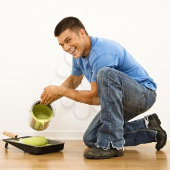 Royalty Free Photo of an Attractive Man Smiling and Pouring Paint into a Roller Pan at Home