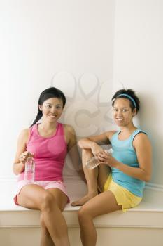 Royalty Free Photo of Two Young Women in Fitness Clothes Holding Water Bottles Sitting Smiling